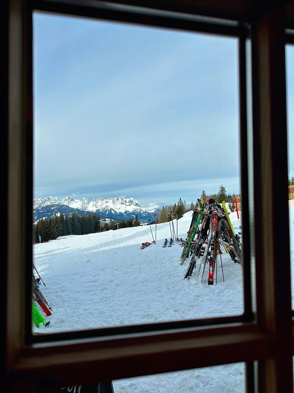 Blick aus einer Hütte auf Skier im Schnee und verschneite Berge